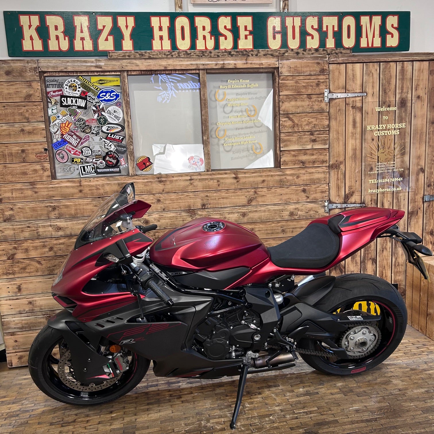 Red and black motorcycle parked in front of a wooden building with 'Krazy Horse Customs' sign.