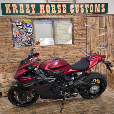 Red and black motorcycle parked in front of a wooden building with 'Krazy Horse Customs' sign.