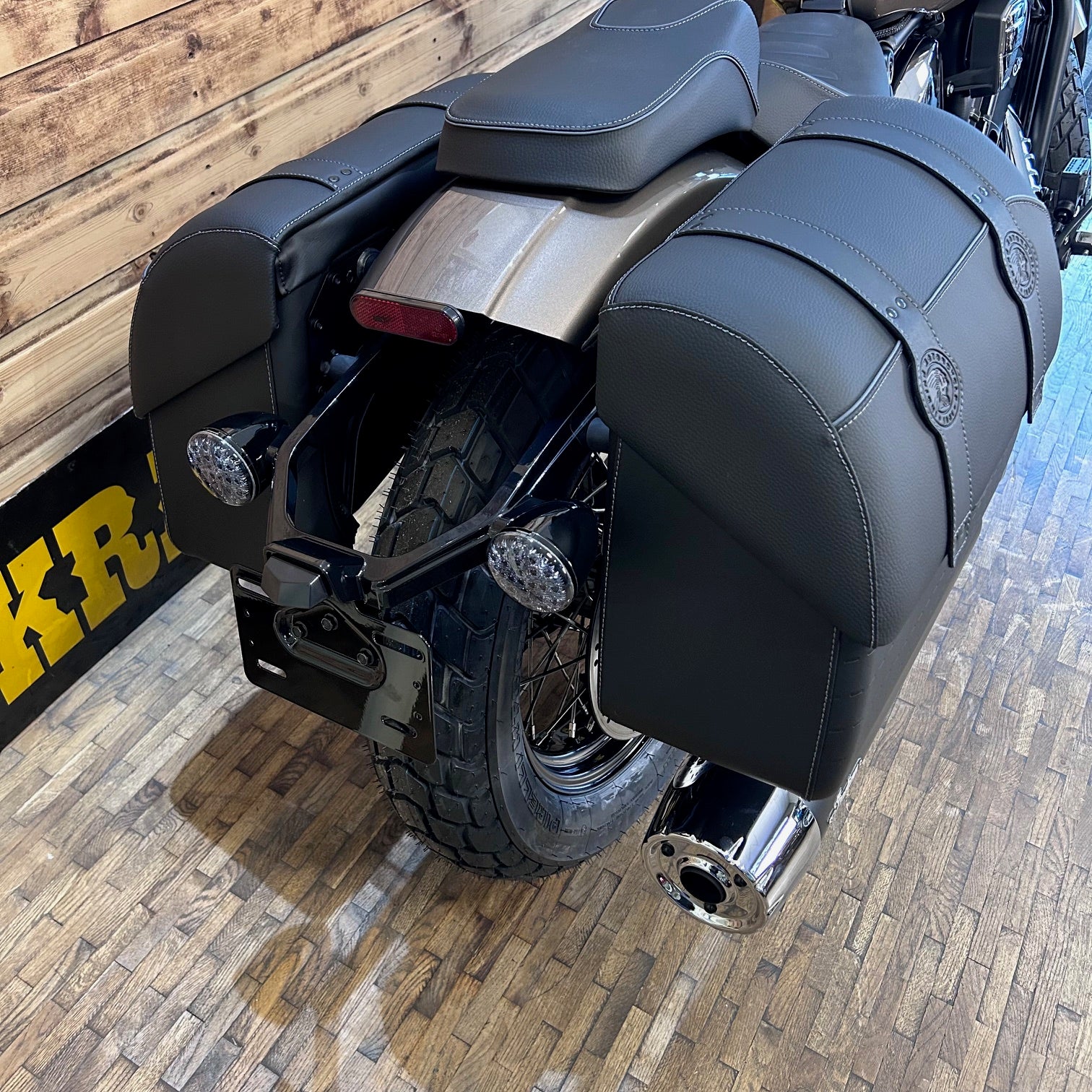 Close-up of a motorcycle's exhaust and rear section on a wooden floor.