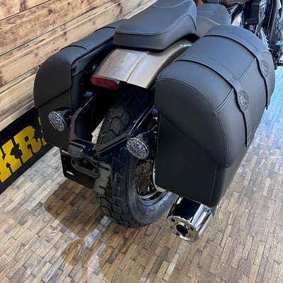 Close-up of a motorcycle's exhaust and rear section on a wooden floor.
