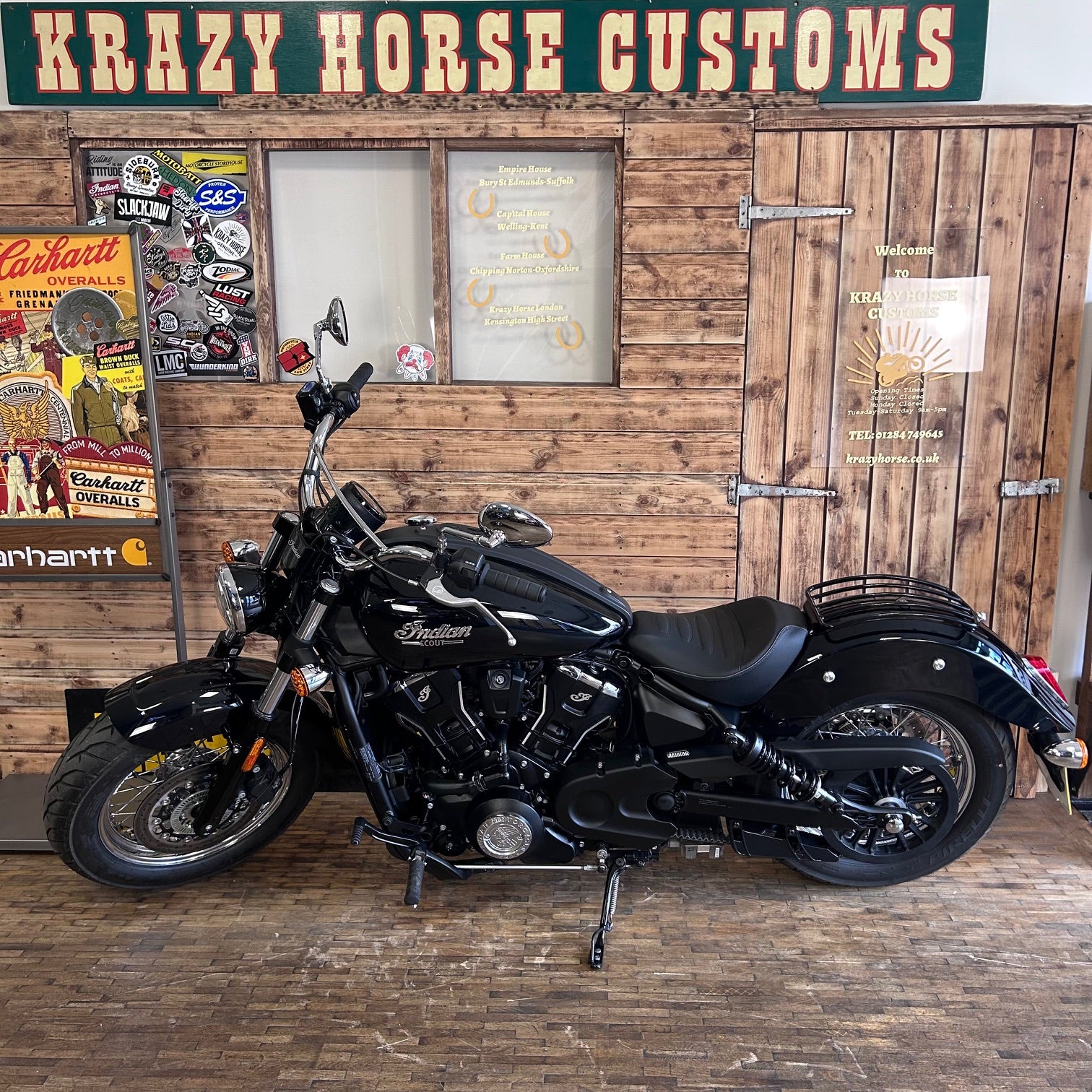 Black motorcycle in a garage with wooden walls and 'Krazy Horse Customs' sign.