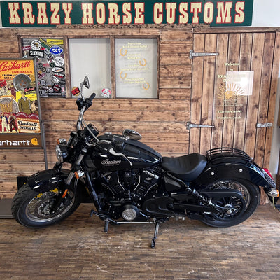 Black motorcycle in a garage with wooden walls and 'Krazy Horse Customs' sign.