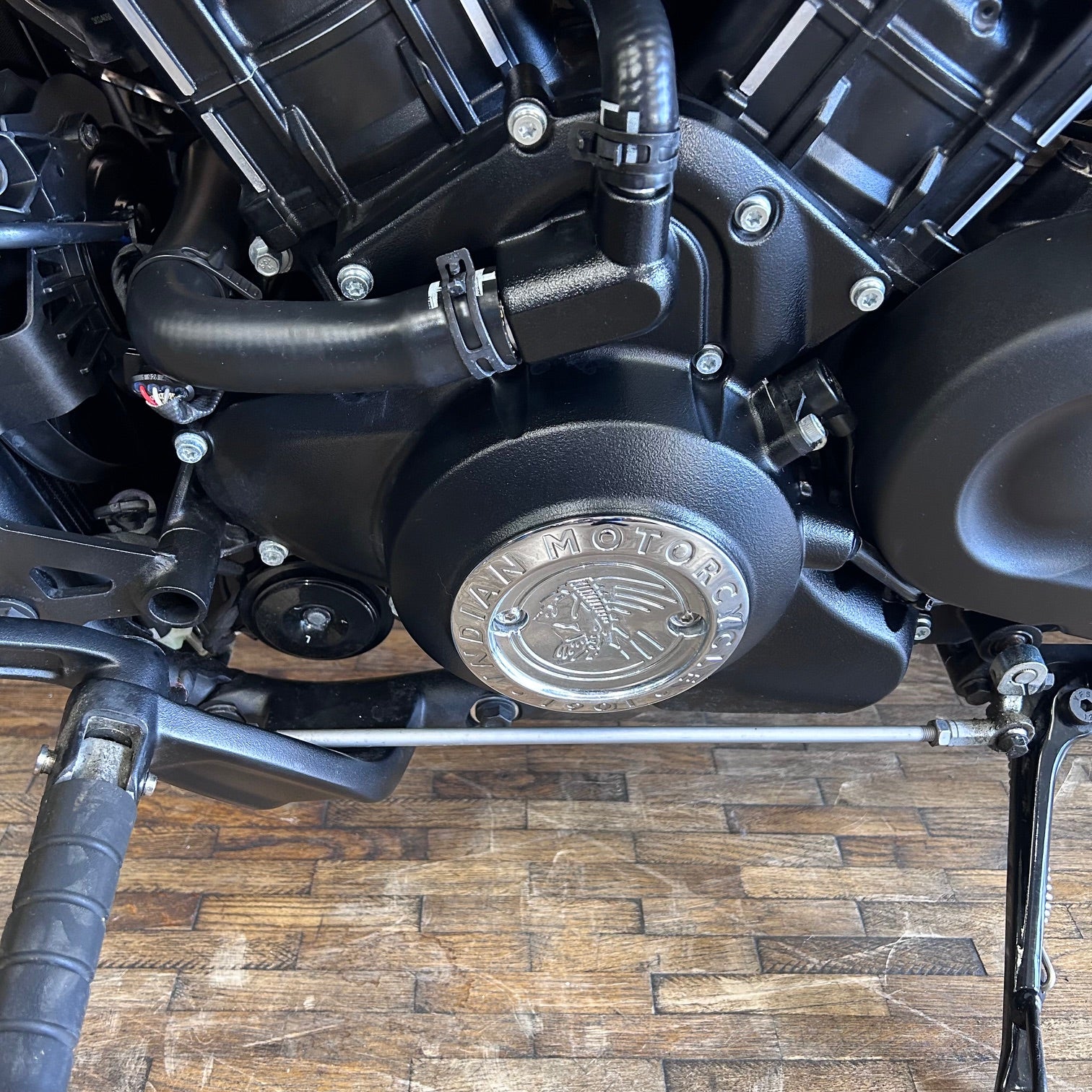 Close-up of a motorcycle engine with 'Indian Motor' branding on a wooden floor.