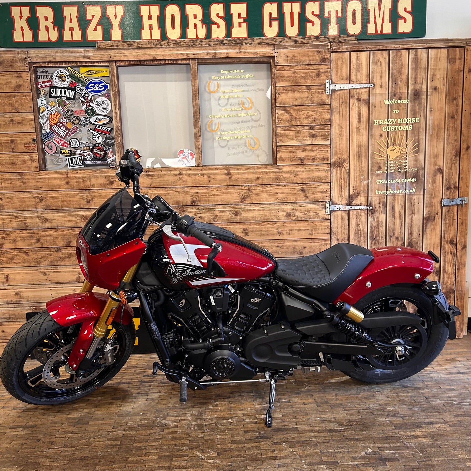 Red motorcycle in front of a wooden wall with 'Krazy Horse Customs' sign.