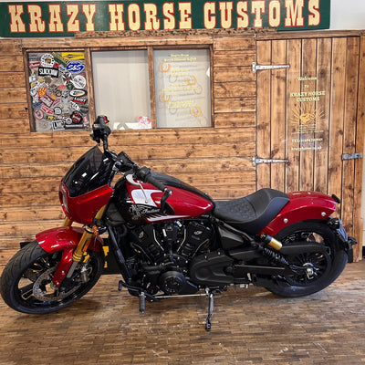 Red motorcycle in front of a wooden wall with 'Krazy Horse Customs' sign.