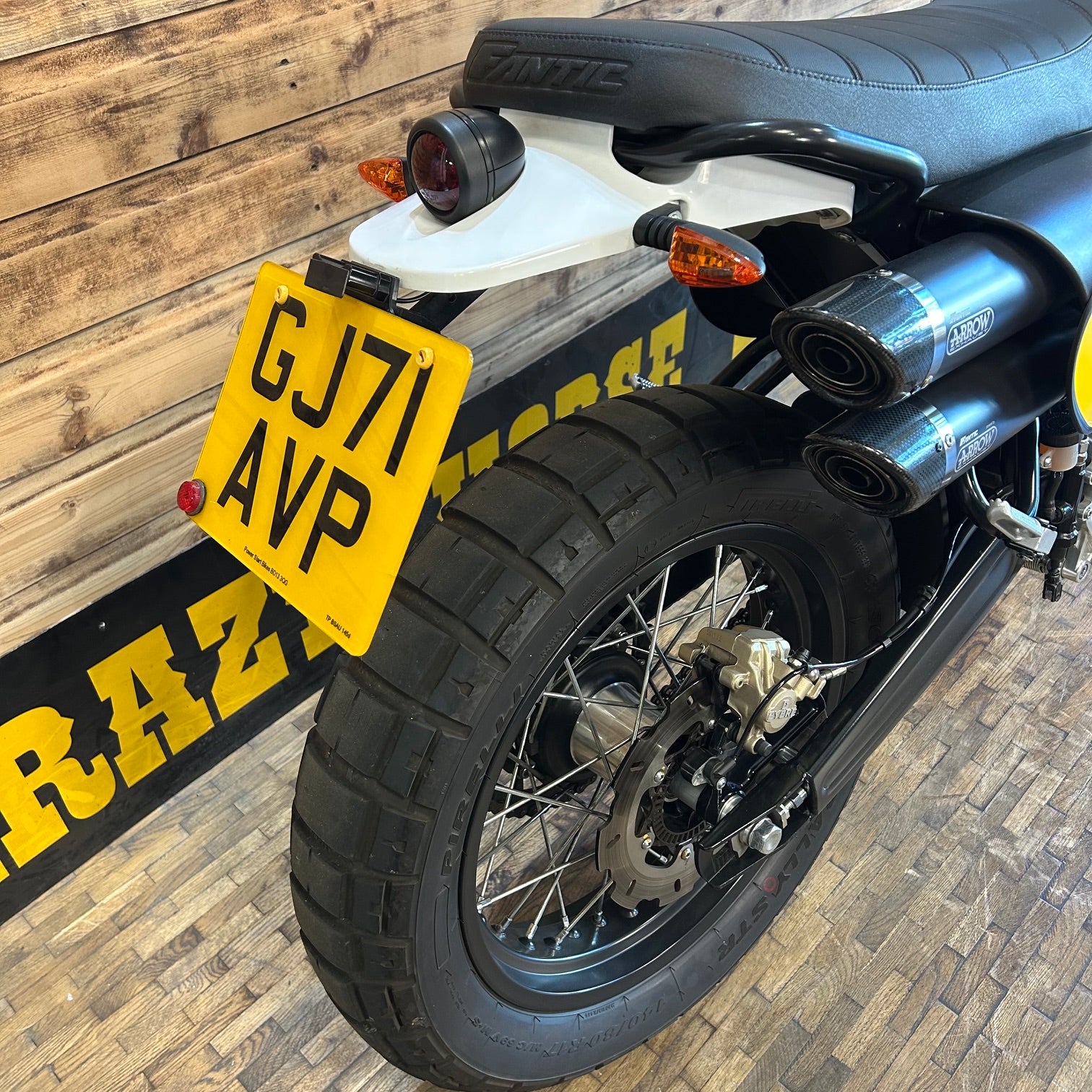 Motorcycle with a yellow license plate against a wooden wall.