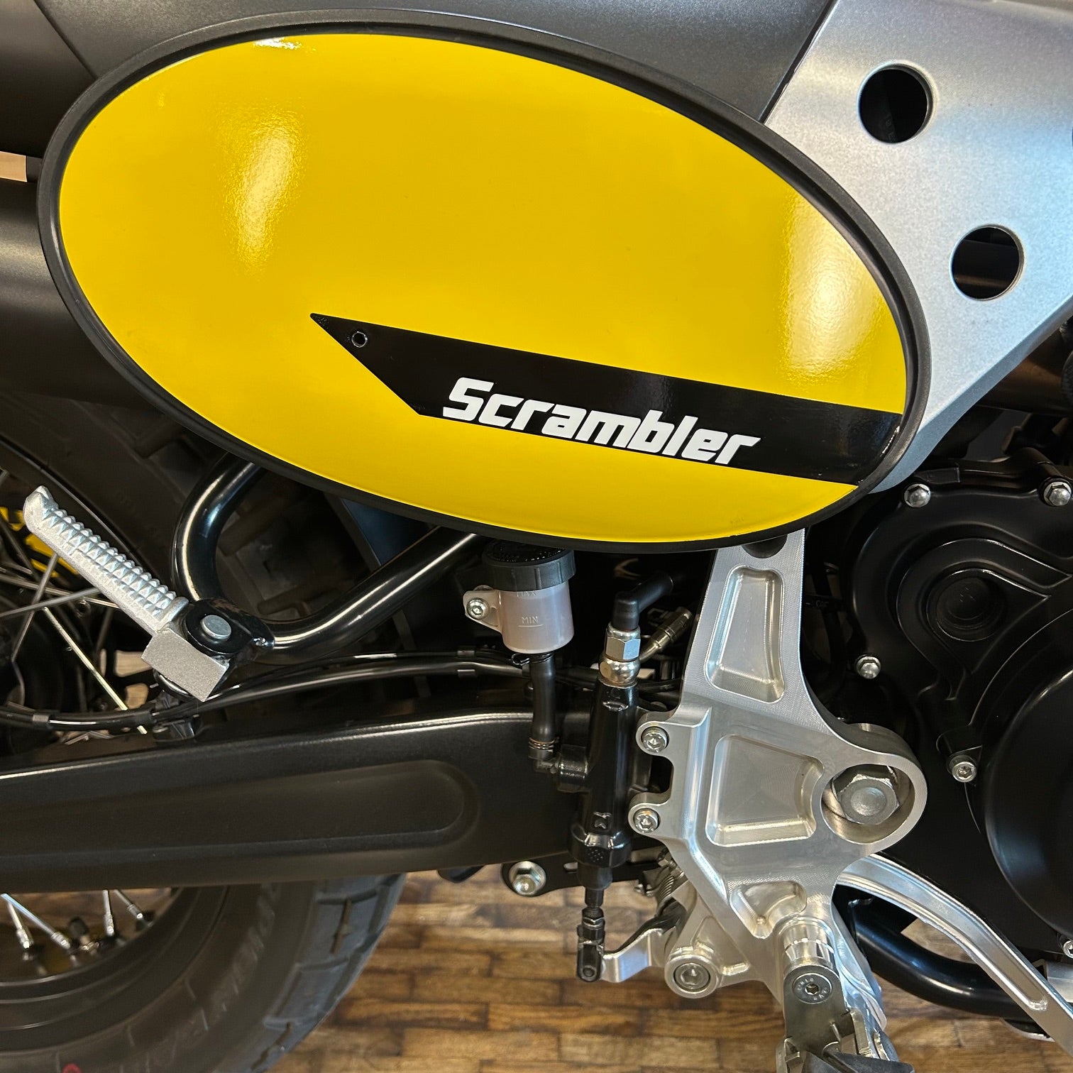Close-up of a motorcycle with a yellow 'Scrambler' exhaust cover.
