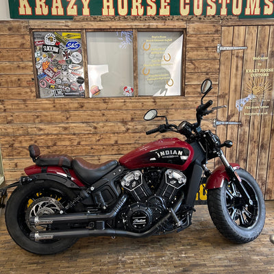 Red Indian motorcycle parked in front of a wooden wall with 'Krazy Horse Customs' sign.
