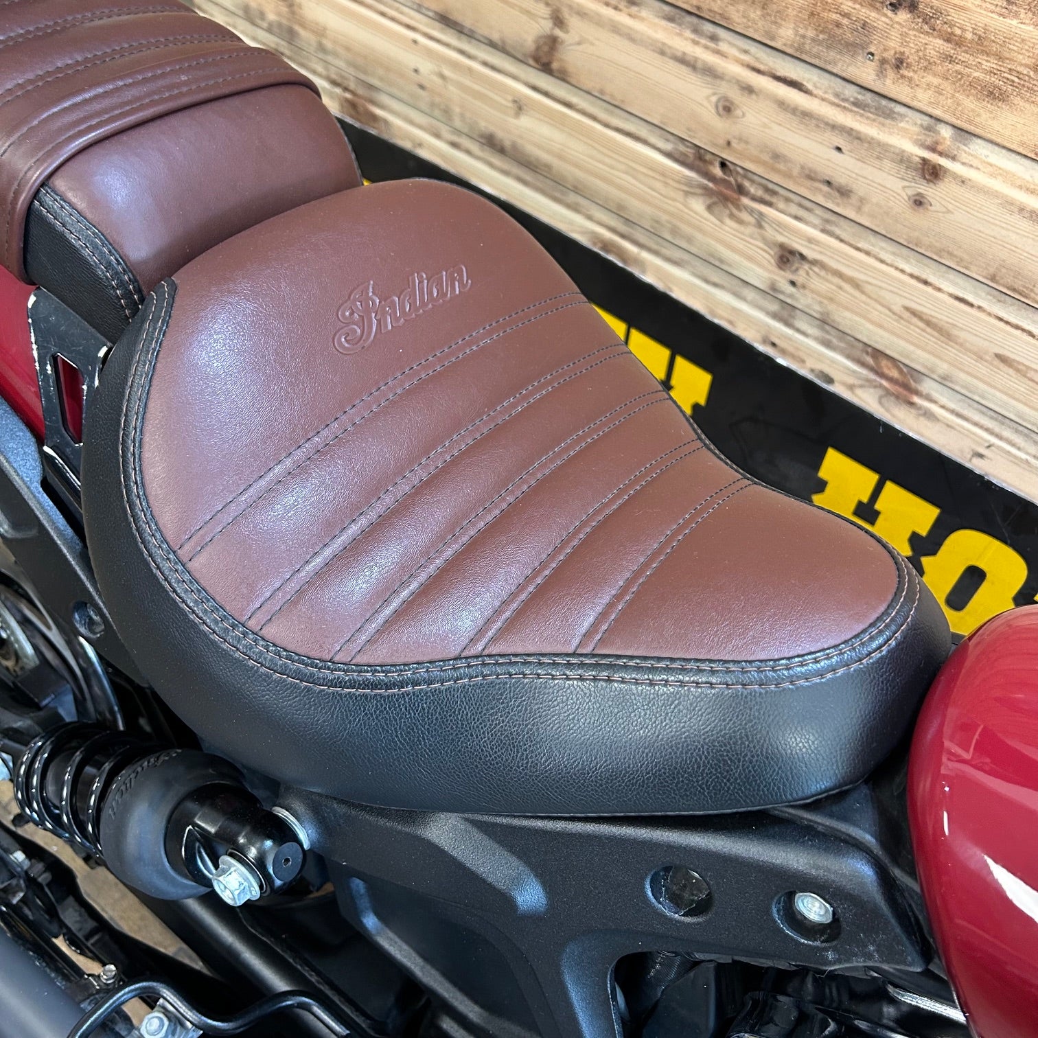 Brown leather seat of a motorcycle with 'Indian' branding against a wooden background.