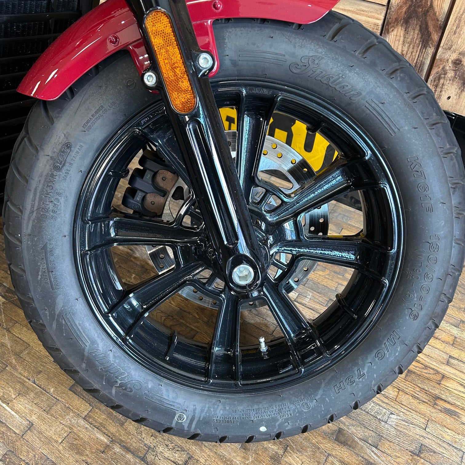 Close-up of a motorcycle tire with a black rim on a wooden floor.