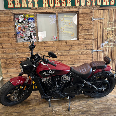 Red Indian motorcycle parked in front of a wooden building with signs.