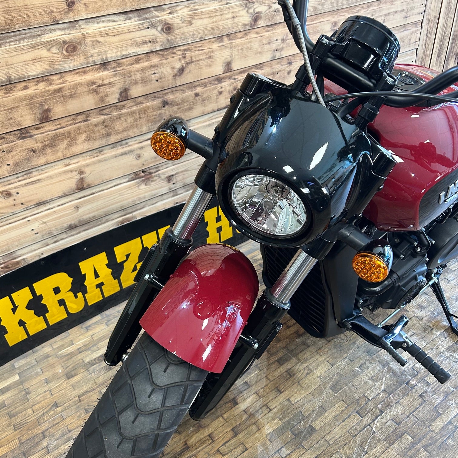 Motorcycle with red fuel tank and black frame on a wooden floor.