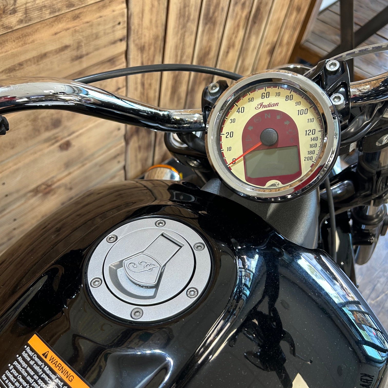Close-up of a motorcycle's handlebar with speedometer and fuel cap against a wooden background