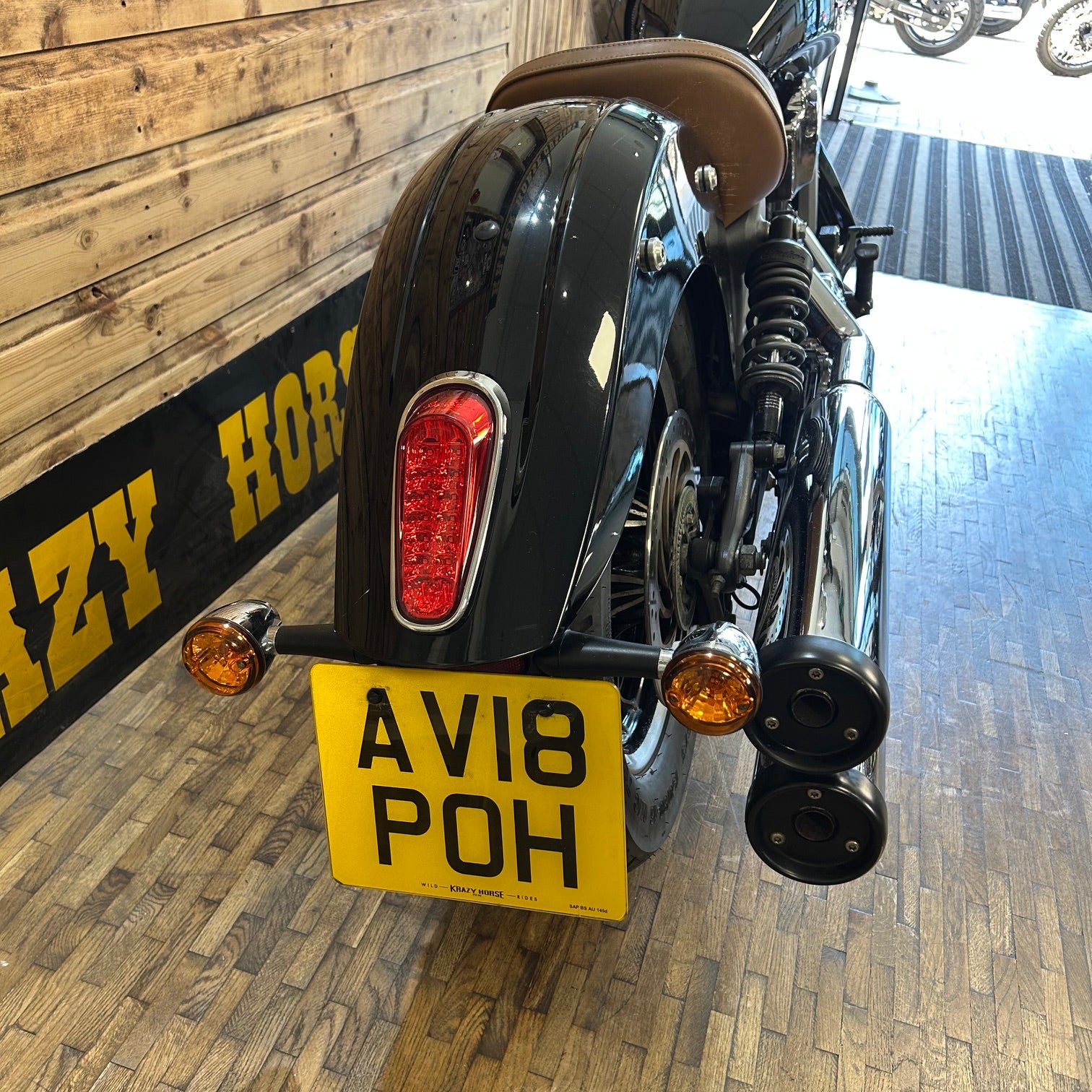 Motorcycle with a license plate 'AV18 POH' on a wooden floor.