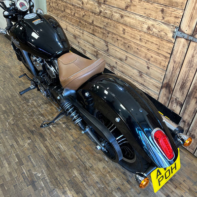 Black motorcycle with brown seat against a wooden wall.