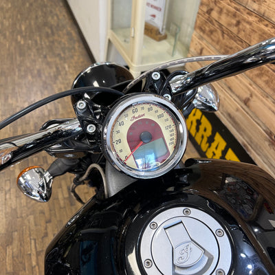 Close-up of a motorcycle's handlebar with speedometer and brand logo.