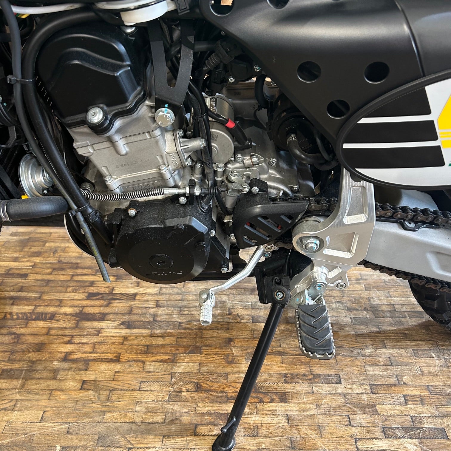 Close-up of a motorcycle engine and chain on a wooden floor