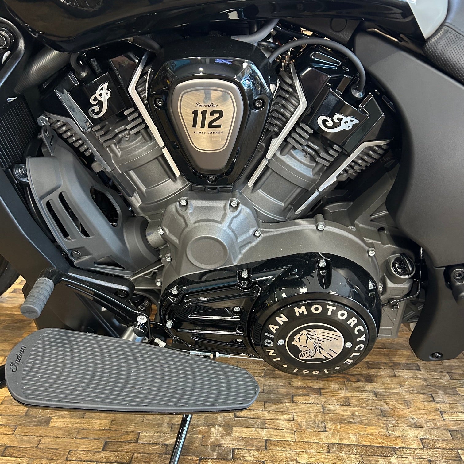 Close-up of a motorcycle engine with 'Indian Motorcycle' branding on a wooden floor.