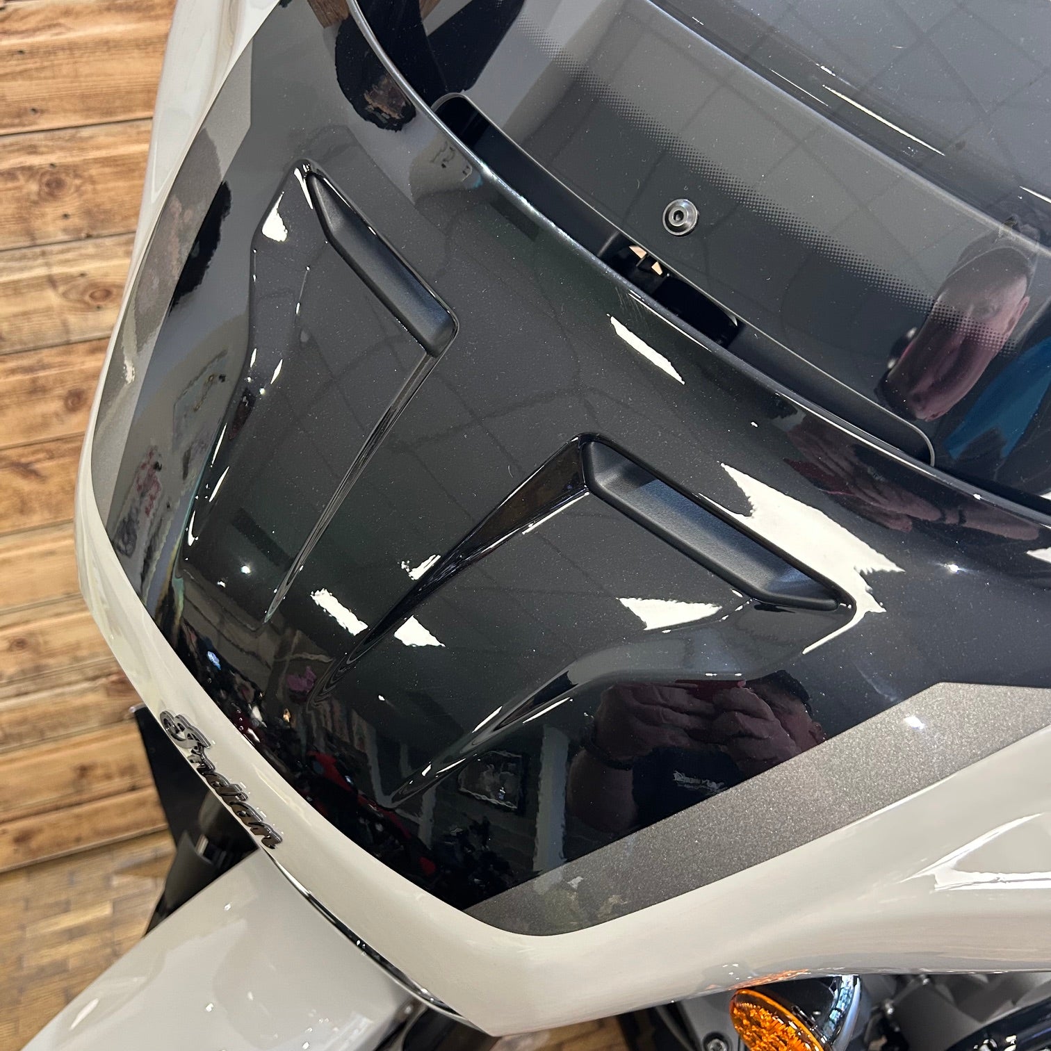 Close-up of a motorcycle's headlight and front fender with a wooden floor background.