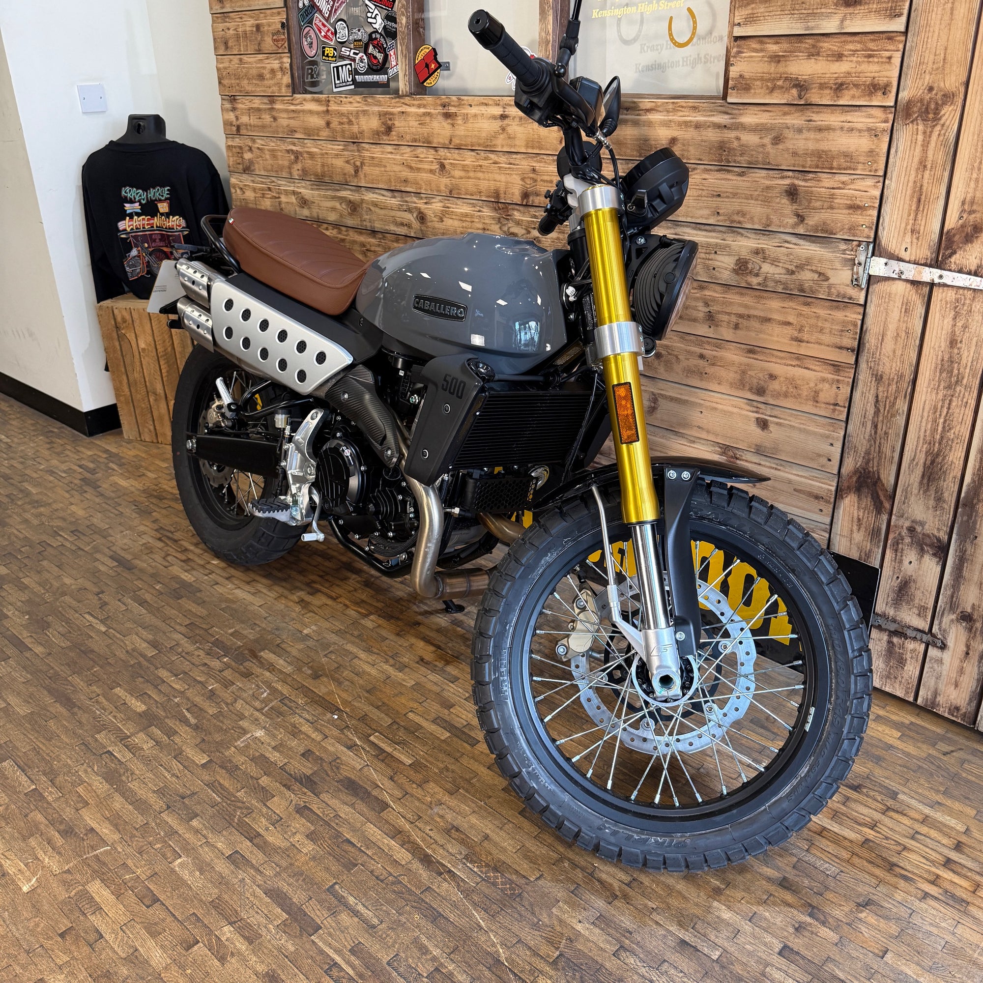 Motorcycle with gold front fork on a wooden floor against a wooden wall.