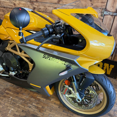 Yellow and gray motorcycle with 'Superveloce' branding on a wooden floor.