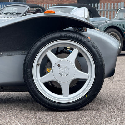 Close-up of a car wheel with a visible brand logo on a road.