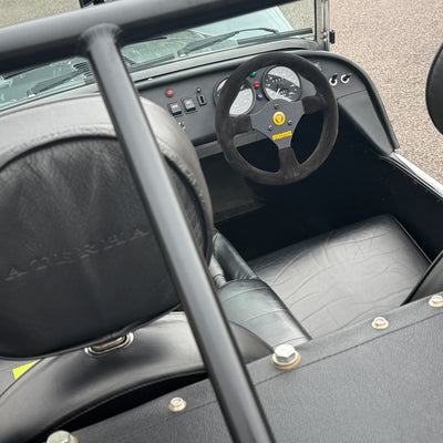Close-up of a car interior with steering wheel and dashboard, featuring the Maserati logo.