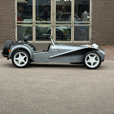 Silver sports car parked in front of a brick building with large windows.
