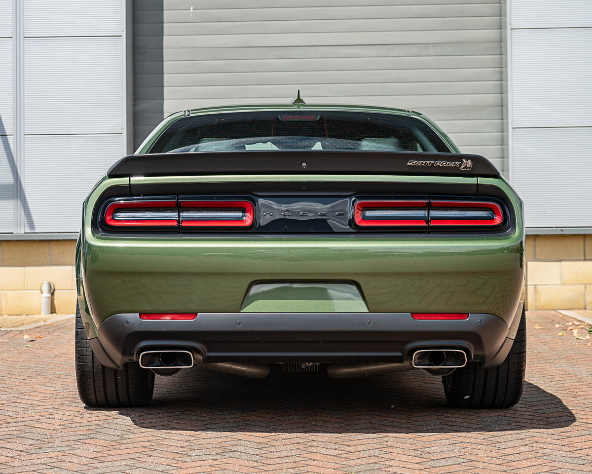 Green Dodge Challenger rear view with red taillights against a gray wall.