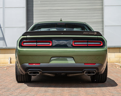Green Dodge Challenger rear view with red taillights against a gray wall.