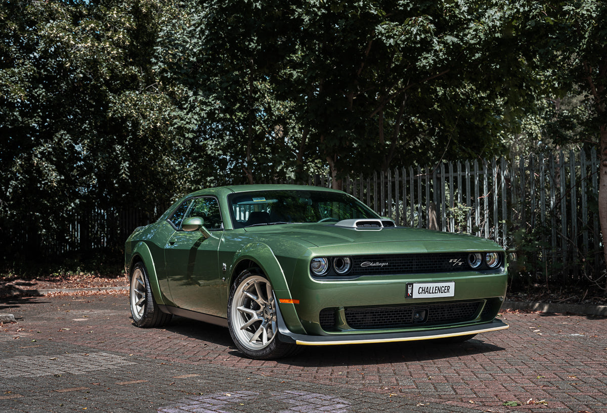Green muscle car parked on a driveway with trees in the background