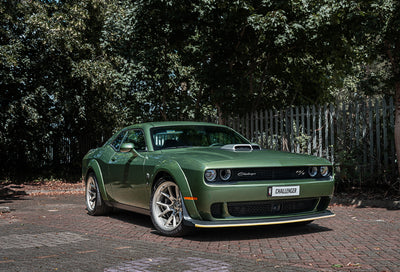 Green muscle car parked on a driveway with trees in the background