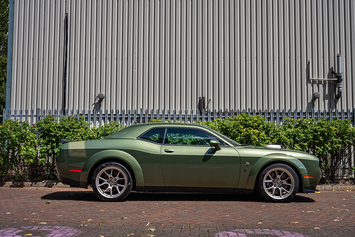 Green sports car parked in front of a metallic building with greenery.