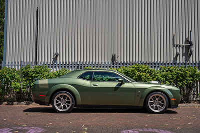 Green sports car parked in front of a metallic building with greenery.