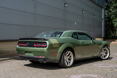 Green sports car parked on a paved area with a gray building in the background