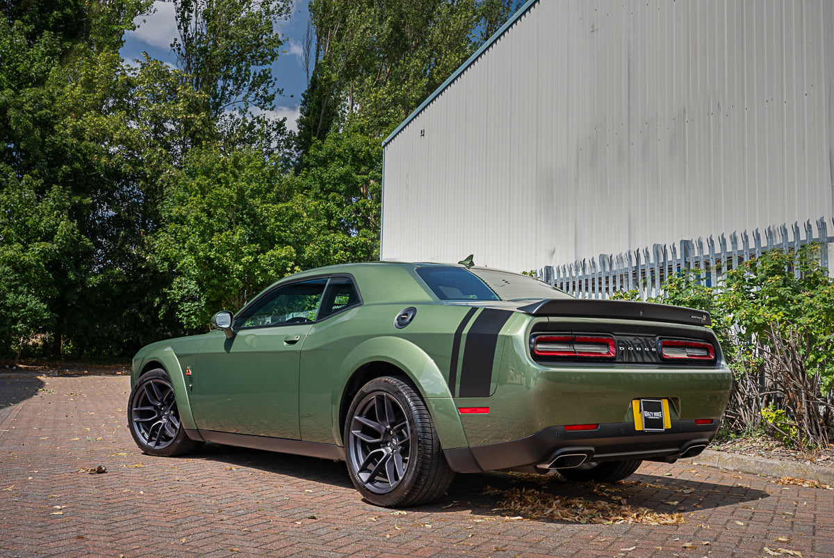 Green muscle car parked on a brick driveway with trees and a building in the background