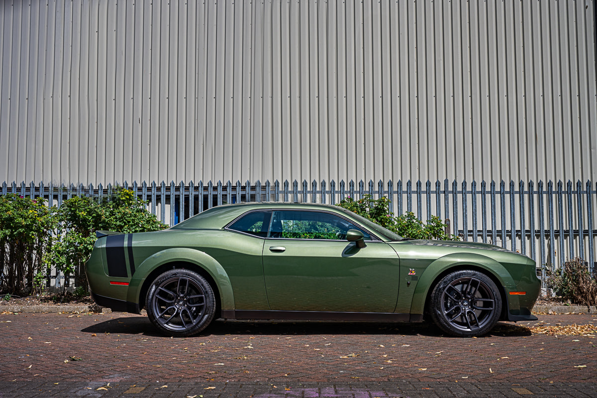 Green muscle car parked in front of a metal fence
