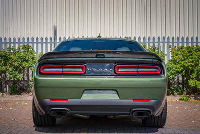 Green Dodge car with red taillights parked in front of a white building.