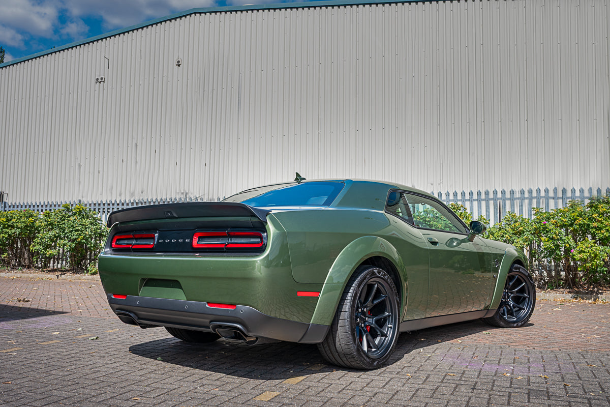 Green muscle car parked in front of a building with a clear sky.