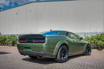 Green muscle car parked in front of a building with a clear sky.