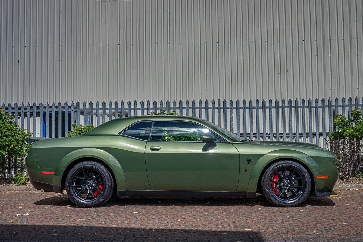 Green muscle car parked in front of a metal fence