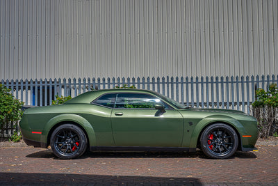 Green muscle car parked in front of a metal fence
