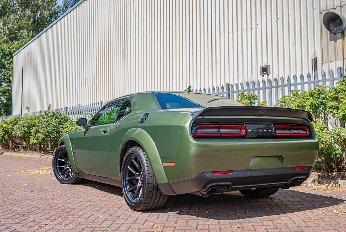 Green muscle car parked on a brick driveway with a building in the background
