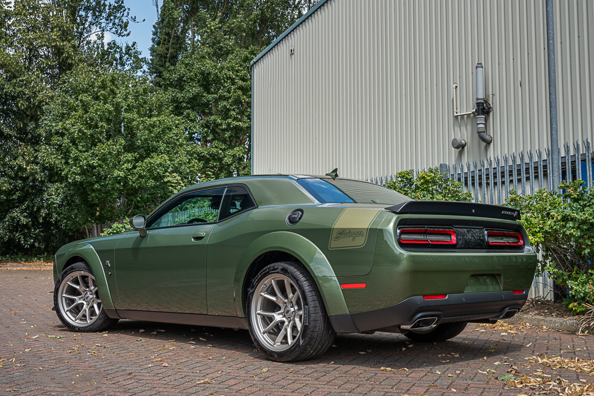 Green muscle car parked on a driveway with trees and a building in the background
