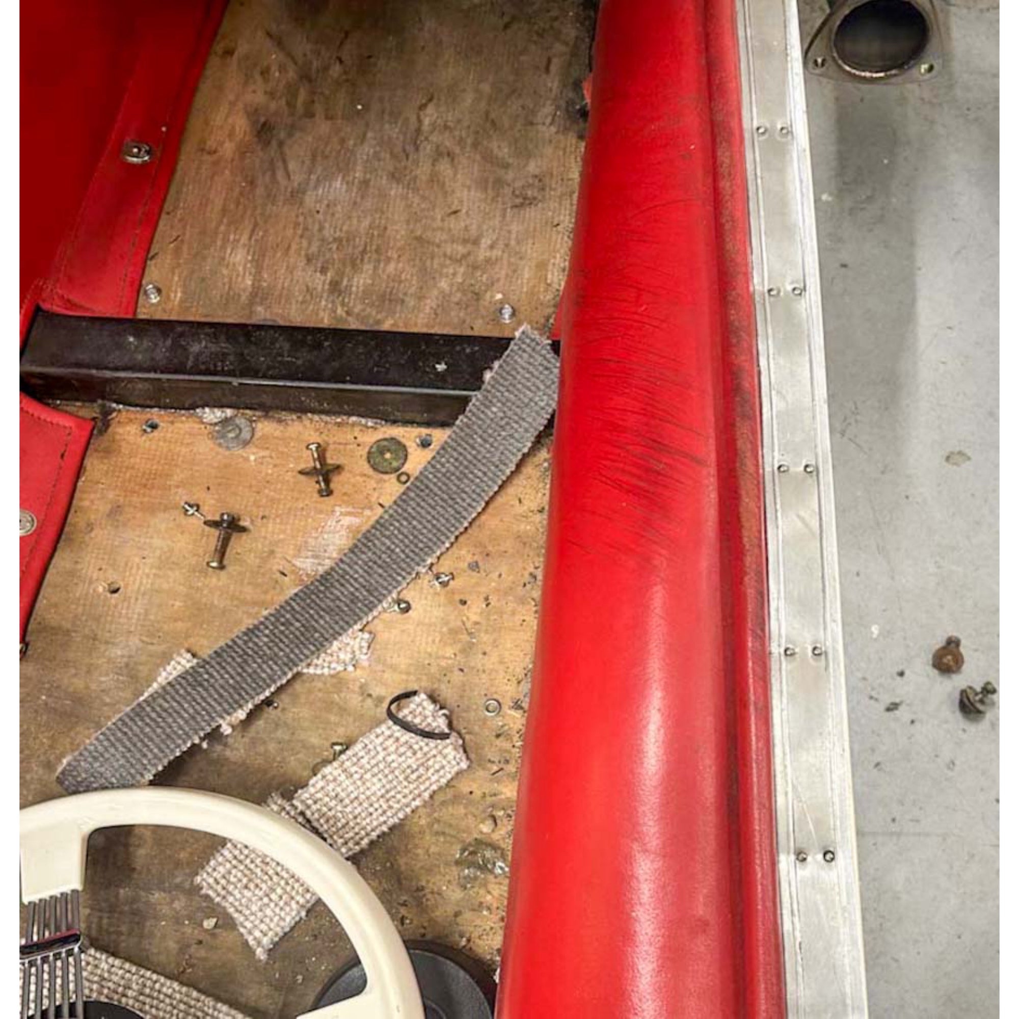 Close-up of a red cylindrical object on a wooden surface with tools and metal pieces.