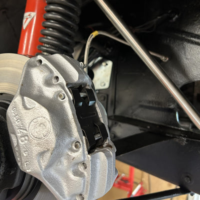 Close-up of a car brake caliper with visible branding in a workshop setting.