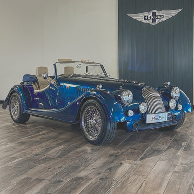 Blue vintage car on a wooden floor with a branded wall in the background
