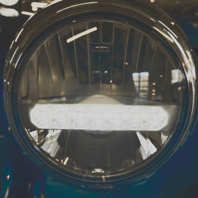 Close-up of a round headlight with a metallic finish on a vehicle.
