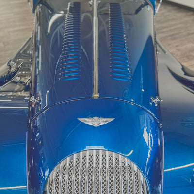 Close-up of a blue vintage car's hood with a prominent emblem.