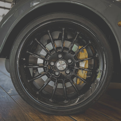 Close-up of a black car wheel with yellow brake caliper on a wooden floor.